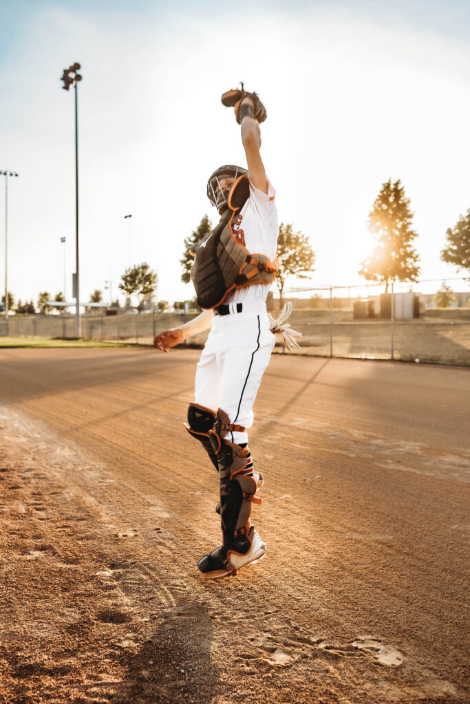 Action shot of a high school baseball catcher in full gear, prepared for the pitch, captured during an 'In Action' photoshoot by Tiffany Chesley Artistry.